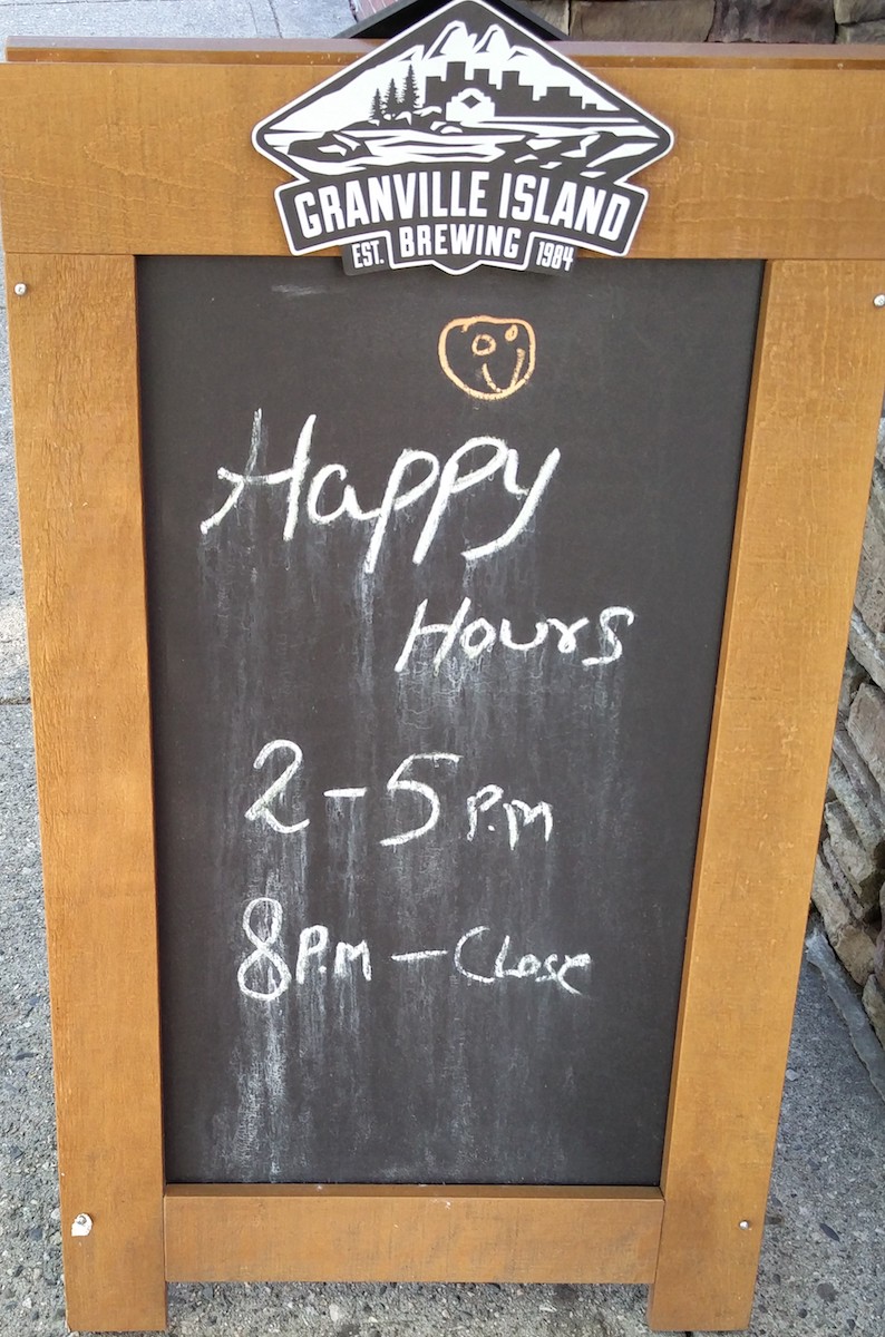 Panneau de bois à l'entrée d'un bar indiquand que le happy hour dure de 2h de l'après midi à 5h du soir.