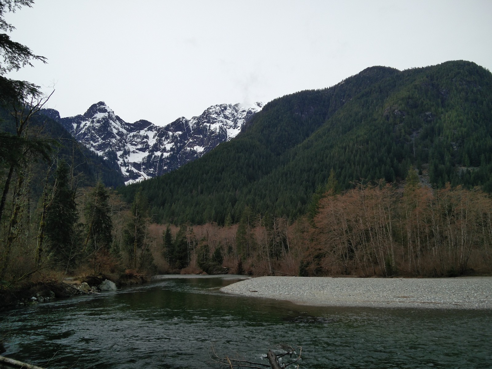 Virage dans la rivière créant une large plage de sable et de gravier sur la rive d'en face, avec des montagnes au dessus et un glacier au loin.